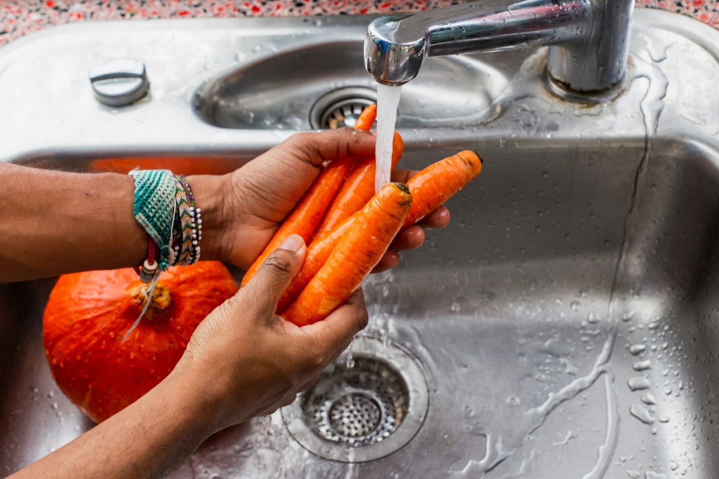Hands rinsing fresh carrots under water — clean food prep representing reduced toxic load