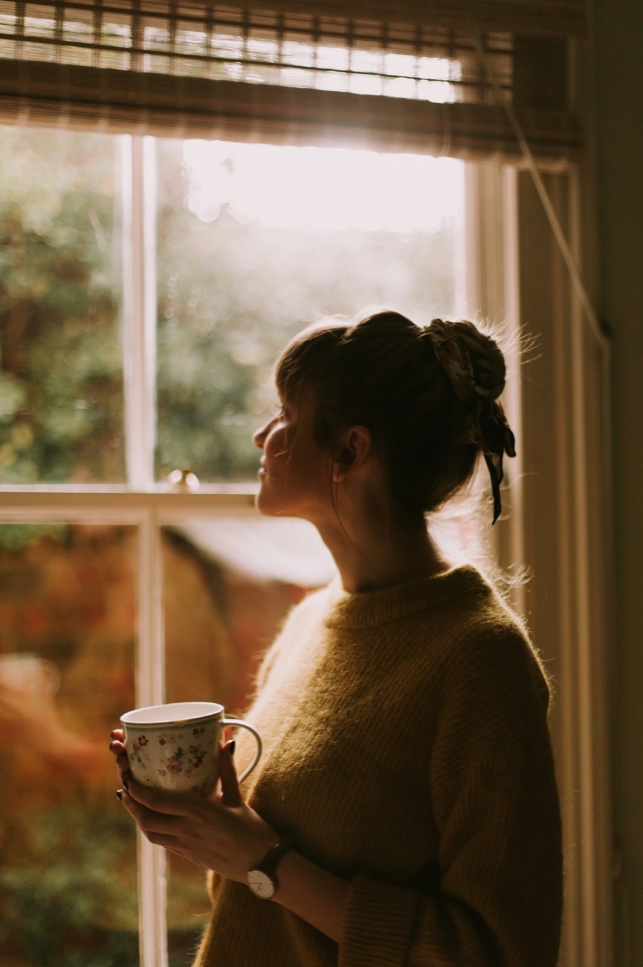 Contemplative woman holding a teacup near a window in soft daylight